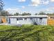 Grey single-story home featuring a spacious, well-maintained lawn bordered by a wooden fence and mature trees at 8303 Croton Ave, Tampa, FL 33619