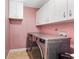 Bright laundry room featuring a pink wall and white cabinets above a washer and dryer at 9445 Preston Rd, Brooksville, FL 34601