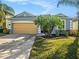 Charming single-story home featuring a well-manicured lawn, a tan garage door, and vibrant tropical landscaping at 13192 Royal Pines Ave, Riverview, FL 33579