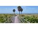 Scenic view of a boardwalk leading to a beach with lush vegetation and clear skies at 13235 Gulf Blvd # 306, Madeira Beach, FL 33708