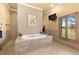 Elegant bathroom with a tiled platform bathtub, wall-mounted TV, and natural light from plantation shutters at 14739 Vista View Ct, Dade City, FL 33523