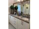 Bathroom vanity area with decorative plants, granite countertops, framed mirror and white cabinets at 1522 Gulf Blvd, Indian Rocks Beach, FL 33785