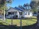 Charming single-story home with a light-colored exterior, blue shutters, and a metal roof, framed by mature trees at 14124 Plum Ln, Hudson, FL 34667