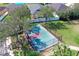 Aerial view of a fenced tennis court surrounded by green spaces and trees in a residential area at 1604 Mira Lago Cir, Ruskin, FL 33570