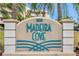 Entrance sign for Madeira Cove with teal lettering and decorative wave accents surrounded by greenery at 399 150Th Ave # 101A, Madeira Beach, FL 33708