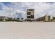 Exterior view from the sandy beach showing a high rise and neighboring buildings under partly cloudy skies at 5396 Gulf Blvd # 110, St Pete Beach, FL 33706