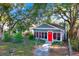 Charming cottage-style home with a vibrant red door, fenced yard, and mature trees at 5518 11Th St, Zephyrhills, FL 33542