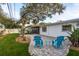 Lovely backyard featuring patio, mature trees, and vibrant blue Adirondack chairs, perfect for outdoor relaxation at 932 Lexington Dr, Dunedin, FL 34698