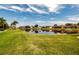 Backyard view of pond surrounded by green grass, palm trees and landscaping at 1115 Signature Dr, Sun City Center, FL 33573