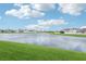 Scenic lake view from the backyard featuring lush green grass and neighboring homes under a bright, cloudy sky at 12829 Tortoise Shell Pl, Riverview, FL 33579