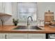 Close-up of a kitchen sink with wood countertops, white cabinets, and a window bringing in natural light at 2008 Harvard Ave, Dunedin, FL 34698