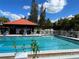 Outdoor pool featuring a red roof pavilion, lounge chairs, and surrounding trees under a partly cloudy blue sky at 3265 Beneva Rd # 202, Sarasota, FL 34232