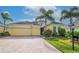 Charming yellow home featuring a brick driveway, well-manicured lawn, and vibrant tropical landscaping with palm trees at 1605 Emerald Dunes Dr, Sun City Center, FL 33573