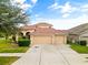 Beige two-story home featuring a three-car garage, tile roof, arched entry, and a well-manicured lawn at 2604 Dakota Rock Dr, Ruskin, FL 33570