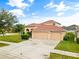 Beige two-story home featuring a three-car garage, tile roof, arched entry, and a well-manicured lawn at 2604 Dakota Rock Dr, Ruskin, FL 33570