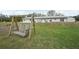 An outdoor wooden swing sits in the backyard of this white single story home with a metal roof at 2040 Underwood Ln, Zephyrhills, FL 33540