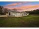 Charming white home featuring large doors, a metal roof, and a spacious green lawn under a beautiful sunset sky at 2040 Underwood Ln, Zephyrhills, FL 33540