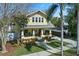 Inviting yellow two-story home featuring a cozy front porch, mature landscaping and long driveway on a sunny day at 445 13Th Ne Ave, St Petersburg, FL 33701