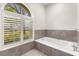 Relaxing bathtub nook featuring an arched window with shutters and stylish gray tiling at 4564 Juniper Dr, Palm Harbor, FL 34685