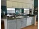 A bright kitchen with white cabinets, gray lower cabinets, stainless steel appliances, and a view into the living room at 11138 Brooklawn Dr, Hudson, FL 34667