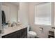 A half bathroom with a dark vanity, toilet, mirror, and window with blinds at 14269 Lemon Yellow Tree Ln, Brooksville, FL 34613