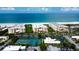 Aerial view showcases beachfront condominiums, tennis courts, and lush landscaping near the ocean at 6500 Sunset Way # 202, St Pete Beach, FL 33706