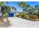 Charming single-story home featuring a paver driveway, lush landscaping, and a bright blue garage door at 11385 9Th E St, Treasure Island, FL 33706