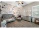 Bedroom features floral wallpaper, a gray crib, accent chair, gray dresser, neutral carpet, and a ceiling fan at 6411 Grenada Island Ave, Apollo Beach, FL 33572