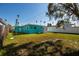 Green backyard showcasing the side of a turquoise home, a storage shed, and partial fencing at 3774 Arkansas Ne Ave, St Petersburg, FL 33703
