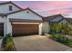 Charming home featuring a brick driveway, two-car garage, and manicured landscaping under a beautiful pink and purple sunset at 17308 Holly Well Ave, Wimauma, FL 33598