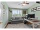 Bright bedroom features a gray sofa, a modern ceiling fan, and a large window with plantation shutters at 112 Brent Cir, Oldsmar, FL 34677