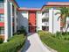 Inviting condo building entrance featuring red doors and tiled roof, surrounded by lush landscaping and white facade at 2612 Pearce Dr # 210, Clearwater, FL 33764