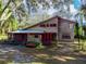 Charming two-story home with a rustic facade, red trim, and a landscaped front yard under a canopy of trees at 12950 Lincoln Rd, Riverview, FL 33578