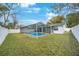 View of the backyard with a screened-in pool, well-manicured lawn, and white fenced perimeter for privacy at 1937 Palm Dr, Clearwater, FL 33763