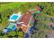 Aerial view showcasing the Beacon Woods East clubhouse, with pool, shuffleboard, and tennis courts in a lush, green setting at 8204 Reynolds Dr, Hudson, FL 34667