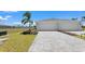 Modern home showcasing a paved driveway leading to a two-car garage with manicured lawn and tropical landscaping at 8069 Shore Lake Dr, Englewood, FL 34224