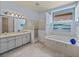 Bright bathroom features a double vanity, tiled shower, and soaking tub with decorative glass block window at 12333 Woodlands Cir, Dade City, FL 33525