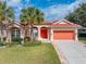 Charming single-story home featuring a red tile roof, an attached two-car garage, and lush tropical landscaping at 12333 Woodlands Cir, Dade City, FL 33525