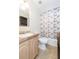 Well-lit bathroom featuring vanity, toilet, shower with decorative curtain, and complementary storage shelving at 36246 Peak St, Zephyrhills, FL 33541