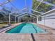 Sparkling pool with screened enclosure, surrounded by a beautiful stone patio and a lush green backyard at 8600 Berkley Dr, Hudson, FL 34667
