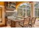 A covered outdoor kitchen featuring stone accents, a stainless steel grill, bar seating, and a mounted television at 4873 Quill Ct, Palm Harbor, FL 34685