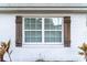 Close-up of exterior brick wall with a window featuring decorative wooden shutters and lush tropical plants below at 13508 Greenleaf Dr, Tampa, FL 33613