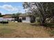 Home's back exterior featuring a screened-in porch and a sprawling grassy yard with mature trees at 6188 Pinehurst Dr, Spring Hill, FL 34606