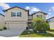 Two-story house with tan siding, two-car garage, and landscaping at 9309 Rally Spring Loop, Wesley Chapel, FL 33545