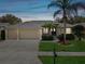 Tan house with three-car garage and palm trees in the front yard at dusk at 8730 Torchwood Dr, Trinity, FL 34655