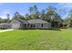 Single-story home with gray siding, a spacious yard, and mature trees surrounding the property at 12040 Pine Warbler Ave, Brooksville, FL 34614