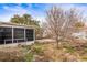 Backyard with screened patio, overgrown grass, and leafless tree at 6333 Sutherland Ave, New Port Richey, FL 34653