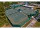 Aerial view of well-maintained tennis courts with green surfaces and shaded seating areas at 11744 Wheatfield Loop, Hudson, FL 34667