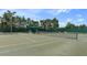 Outdoor tennis court with green surface, net, lighting, and seating area under green awning at 11008 Torrey Pines Ct, Hudson, FL 34667