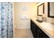 Double vanity bathroom featuring dark cabinets, neutral countertop, mirrors, and a blue seashell shower curtain at 3526 Overland Dr, Holiday, FL 34691